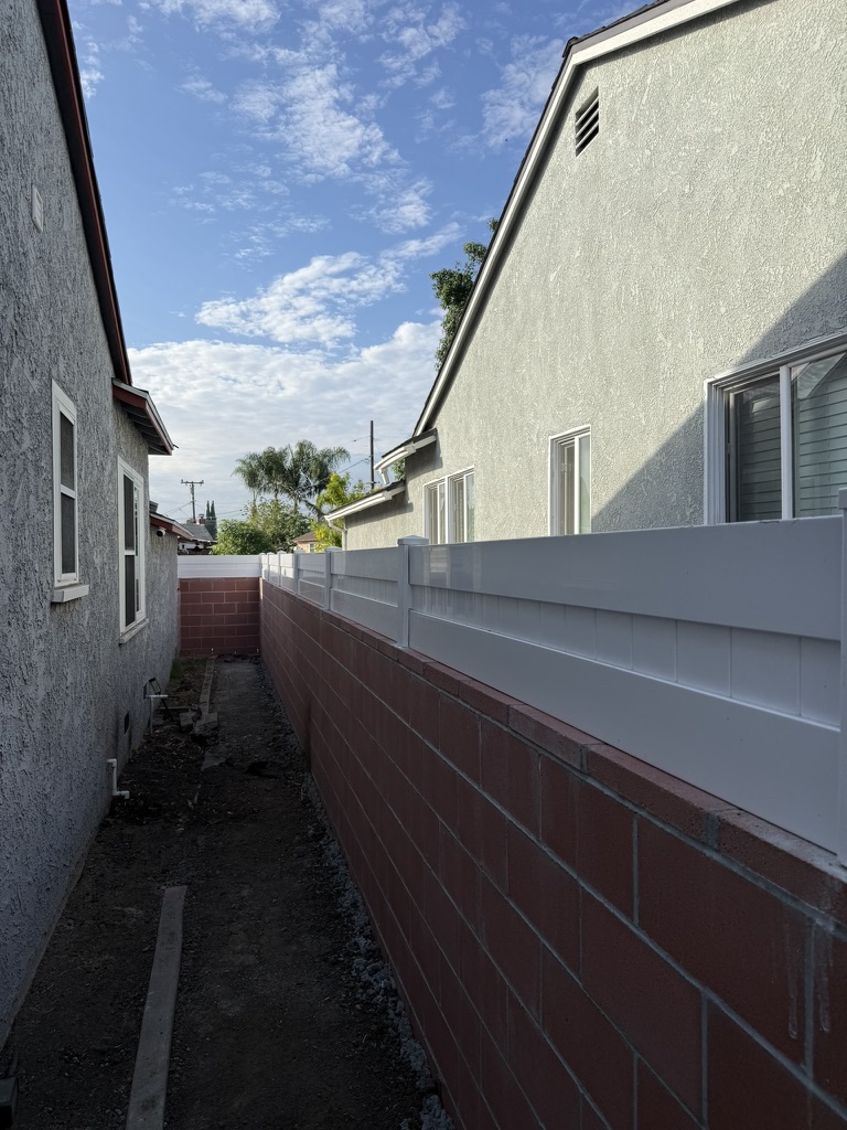 Lanett property after construction with a completed red CMU wall and white vinyl privacy topper